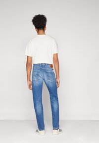Jeans de mezclilla azul con corte recto, lavado claro y detalles sutiles en los bolsillos; combinados con una camiseta blanca y zapatillas casuales.