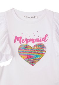 Maglietta bianca con maniche a sbuffo, che presenta la scritta rosa "Mermaid" e un design a forma di cuore con paillettes multicolori in blu, rosa e giallo.