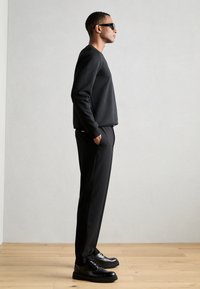 Sweatshirt noir et pantalon à coupe décontractée, associés à des chaussures noires. Le modèle porte des lunettes de soleil, mettant en avant un design minimaliste.