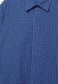 Chemise à carreaux bleue avec col et quatre boutons bleus visibles sur le devant, montrant un motif en grille détaillé.