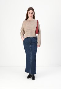 Mehrfarbiger Strickpullover mit Rundhalsausschnitt, kombiniert mit einem dunkelblauen Denim-Maxirock und schwarzen Stiefeletten, trägt eine rote Umhängetasche.