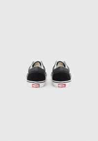 Schwarze Wildleder- und Canvas-Slipper mit weißen Gummisohlen und Nähte. Auffällige rote Markenkennzeichnung an der Ferse.