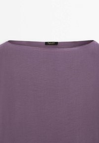 Haut violet léger avec un col large et arrondi. Texture douce avec une finition légèrement froissée. Dispose d'une étiquette près du col.