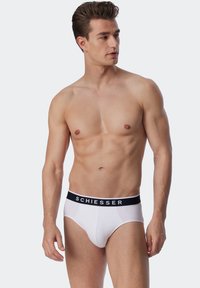 Weiße Baumwollslips mit einem schwarzen elastischen Bund, der mit "SCHIESSER" beschriftet ist. Eng anliegende Form, glatte Textur und minimalistisches Design.