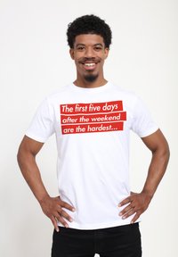 Camiseta de algodón blanca con texto en rojo intenso: "Los primeros cinco días después del fin de semana son los más difíciles..." Manga corta, corte relajado.