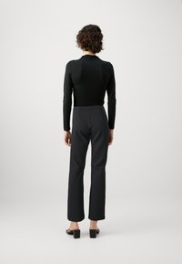 Black long-sleeve top paired with fitted dark pants. Features a slim fit and smooth texture. Chunky black heeled sandals complete the look.