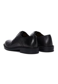 Zwarte leren schoenen met een gladde afwerking, een ronde neus en een lage gestapelde hak. Voorzien van zwarte veters en subtiele stiksels aan de zijkanten.