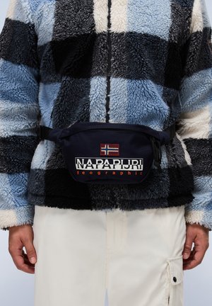 Marsupio blu navy con logo "NAPAPIJRI geographic" e patch con la bandiera norvegese, indossato sopra una giacca in pile a scacchi neri e blu.