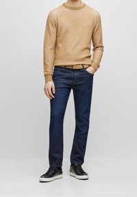 Béžový pletený svetr, tmavě modré džíny a černé tenisky s bílými podrážkami. Oblečení má žebrovanou texturu a volný střih.