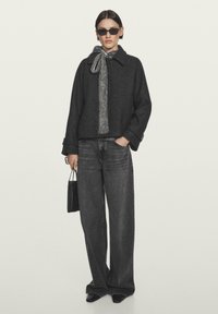 Black wool blend jacket with a collar and a gray knitted scarf, paired with high-waisted, wide-leg gray jeans and black accessories.