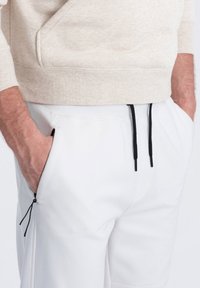 Lichtbeige sweatshirt met een gestructureerde afwerking, gecombineerd met witte broek met zwarte trekkoorden en ritszakken.