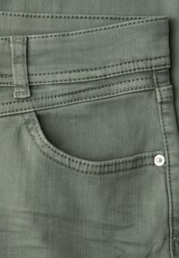 Primo piano di tessuto in denim verde che mostra la tasca frontale, il passante per la cintura e i dettagli delle cuciture visibili.