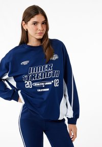 Sudadera navy con acentos blancos, que presenta un gráfico de "FORTALEZA INTERIOR" y un ajuste relajado, combinada con pantalones navy a juego.