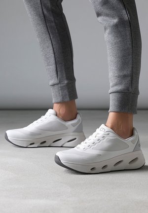 Des chaussures de sport blanches présentent une tige en maille, une semelle rembourrée et un design épuré avec des accents gris et un bout arrondi.