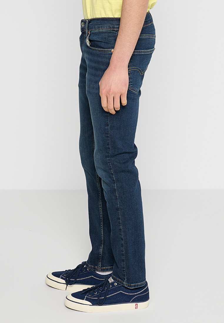 Schmal geschnittene dunkelblaue Jeans aus Denim mit einem leichten Stretch, mit einem Fünf-Taschen-Design und gelben Nähten. Dazu passen marineblaue Sneakers.
