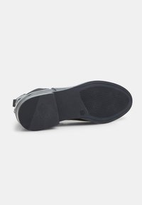 Suela de zapato negra con agarre de goma texturizada, diseño curvado, talón reforzado y material superior liso que se extiende hasta un cierre de cremallera.