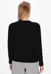 Schwarzer Strickpullover mit geripptem Kragen, gemusterten Zopfstrickärmel und lockerer Passform. Die Textur ist weich und leicht dick.