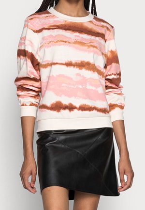Kobieta ubrana w różową, brązową i białą koszulkę z nadrukiem tie-dye z długim rękawem, połączoną z czarną skórzaną mini spódniczką.