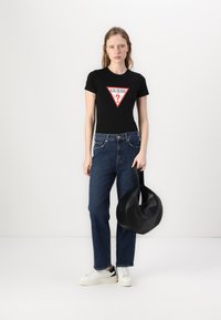 Camiseta negra ajustada con logo triangular rojo y blanco; jeans rectos azules; bolso circular negro; zapatillas blancas con acentos negros.