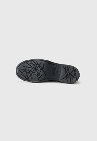 Semelle de chaussure noire en caoutchouc présentant un motif texturé avec des lignes entrecroisées et un logo. Les bords courbés et les accents de design surélevés sont visibles.