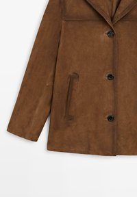 Giacca in suede marrone con colletto a lancia, design monopetto e bottoni neri. Presenta una tasca laterale e una texture liscia.