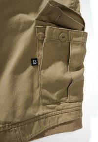 Khaki szövet elülső zsebbel, gombbal záródó. Kis fekete címke fehér "B" betűvel. Texturált pamut anyag.