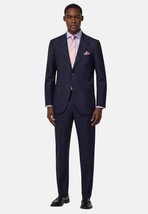 Navy-Anzug mit einem taillierten Sakko mit Revers, zwei Knöpfen und Seitentaschen. Kombiniert mit einem hellblauen Hemd und einer rosa Krawatte.