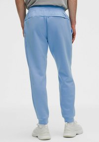 Sv�ětlé modré tepláky s volnějším střihem, vyrobené z měkké látky. Mají zadní kapsu a žebrované manžety. Kombinovány s bílými teniskami.