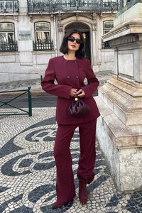 Bordo izgriezts uzvalks ar divrindas žaketi un platām biksēm. Aksesuāri ietver taisnstūrveida saulesbrilles un mazu brūnu rokassomu.