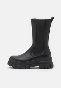 Botas negras de tobillo con parte superior de cuero suave y paneles laterales elásticos. Suela de goma gruesa con una banda de rodadura robusta para mayor tracción.
