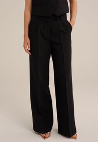 Črne široke hlače z gladko teksturo, ki imajo stranske žepke in prilagojen kroj, dopolnjene z oprijetim jopičem in sandali z odprto konico.