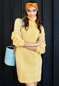 Abito maglione giallo a trecce con colletto alto, coppia di bottoni sulle maniche e una borsa a secchiello blu con accenti marroni.