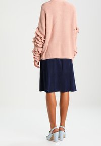 Różowy prążkowany sweter z falbanami na rękawach, zestawiony z granatową spódnicą do kolan i jasnoniebieskimi sandałami na szerokim obcasie.