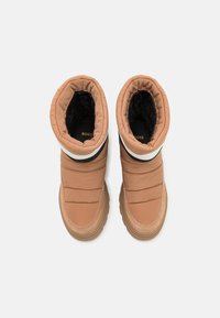 Brązowe, puchate buty z pikowanej tekstury, z czarno-białymi akcentami, miękką podszewką i grubą, gumową podeszwą zapewniającą przyczepność.