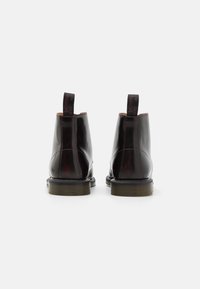 Černé kožené kotníkové boty s lesklým povrchem, kulatou špicí a texturovanou gumovou podrážkou. Obsahují zadní poutka s detailem loga.