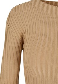 Pull en maille côtelée beige avec manches longues et col rond haut, montrant une texture tricotée verticale détaillée.