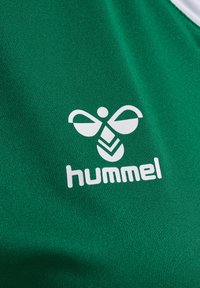 Green textile with a smooth texture featuring a white logo consisting of a stylized bee and the word "hummel" below it.