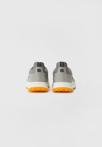 Baskets de sport grises et noires avec une semelle en caoutchouc orange texturé. Présentent un dessus lisse et des détails de talon renforcés.