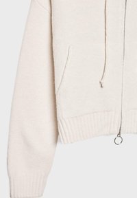 Jasnobeżowa bluza z kapturem na zamek, wykonana z miękkiego materiału. Posiada ściągacze przy mankietach i u dołu, sznurki oraz kieszenie z przodu. Gładka tekstura z minimalnymi detalami.