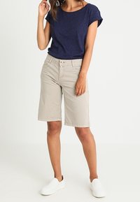 Marinblå t-shirt med kort ärm och beiga knälånga shorts, med knappstängning, bärs med vita slip-on skor. Slät tyg och avslappnad passform.