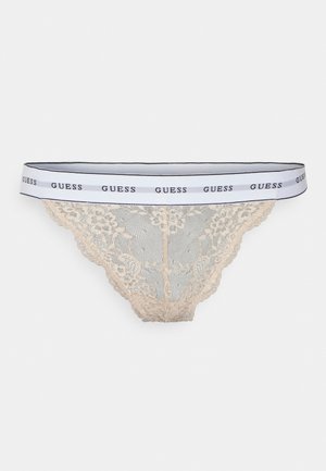 Tanga de encaje en tono nude con una cinturilla de marca en blanco y negro que presenta la palabra "GUESS". Patrón floral de encaje intrincado, textura suave.
