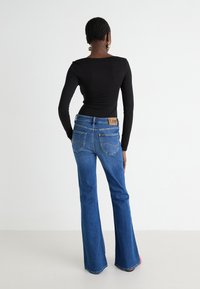 Maglietta nera a maniche lunghe abbinata a jeans a zampa d'elefante blu con una patch in pelle marrone Lee sul retro. Tessuto liscio con cuciture dettagliate.