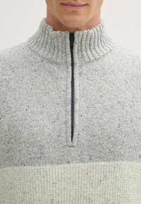 Grijze gebreide trui met een hoge kraag en ritssluiting. Heeft een gestructureerde afwerking en een contrasterende lichtgrijze horizontale streep.