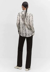 Langärmlige Bluse im beige-grauen Schlangenprint, mit Kragen und geknöpften Manschetten, kombiniert mit schwarzen Hosen mit weitem Bein.