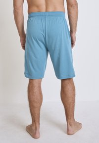 Blaue Baumwollshorts mit einem elastischen Bund, ausgestattet mit einem schlichten Design und umsäumten Säumen, von hinten betrachtet.