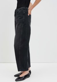 Jeans in denim nero con un design a gamba dritta, caratterizzati da tasche laterali e vita alta. Abbinati a ballerine nere, che mostrano una texture liscia.