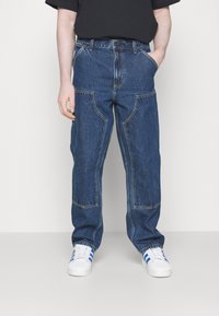 Blaue Jeans aus Denim mit lockerer Passform, kontrastierenden Nähten, Fronttaschen und einem hohen Taillendesign, kombiniert mit weißen Sneakers.