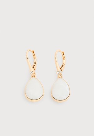 Cercei lungi de culoare aurie cu pietre albe în formă de lacrimă și cristale clare mici deasupra închizătorilor, pe un fundal deschis.