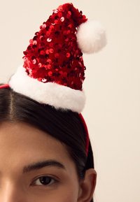 Red sequined Santa hat with a white faux fur trim and a pom-pom at the top, mounted on a red headband. Shiny and textured design.
