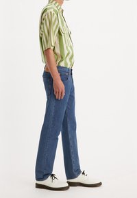 Kortärmad skjorta med gröna och krämfärgade vertikala ränder, kombinerad med blå raka jeans och vita snörskor med svarta snören.